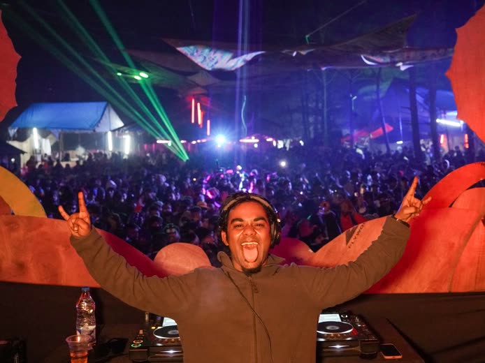 Protonix on stage at an open-air psytrance festival, arms raised